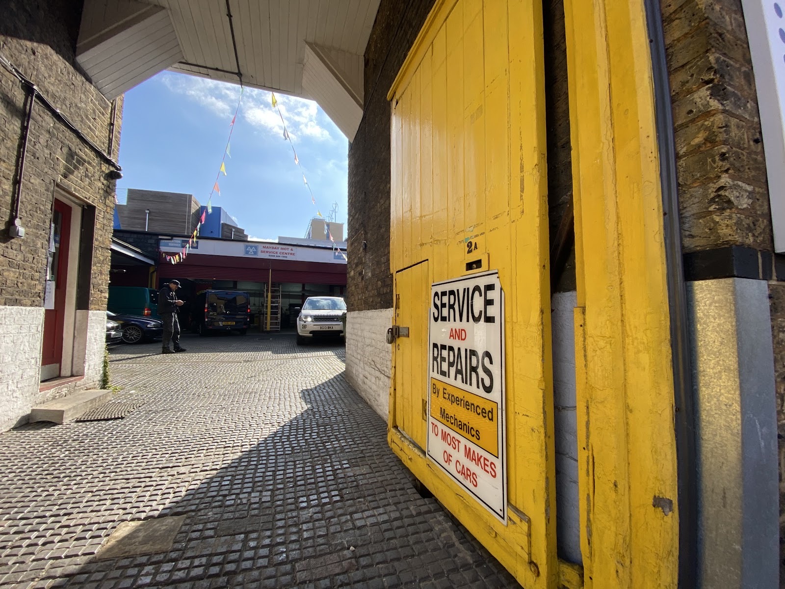 A white Rolls-Royce raised on the ramp inside Mayday MOT and Service Centre on A Mayday Rd, under the workshop sign